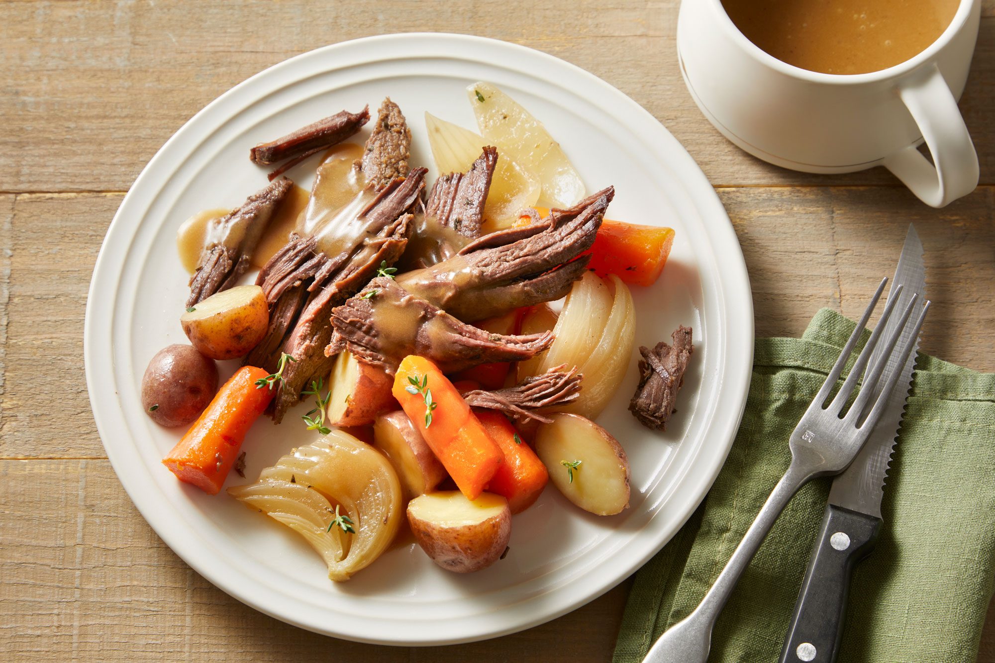 Overhead shot of Venison Roast; served in a plate; top with sauce; spoon and fork nearby over green tablecloth; all set on wooden surface