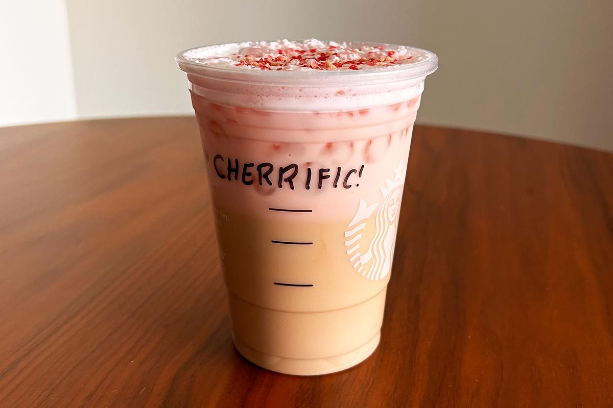 Starbucks iced cherry chai drink with "Cherrific!" written in sharpie on the cup, on a wooden table