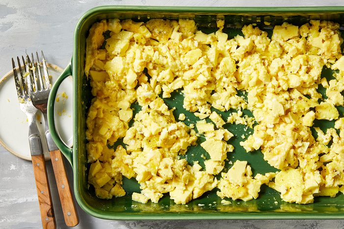 A green baking dish filled with scrambled eggs sits on a gray surface.