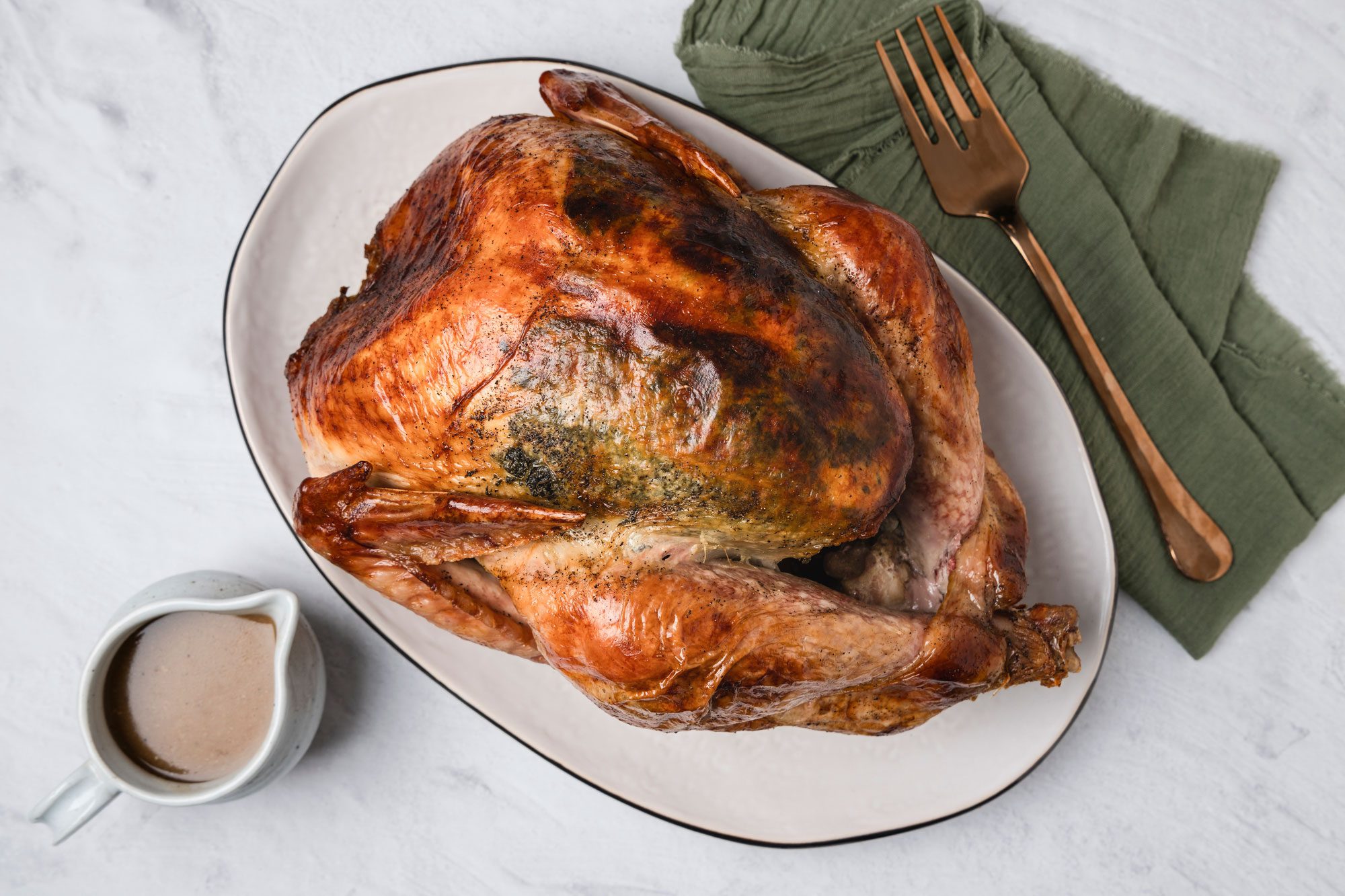 Overhead shot of Classic Cheesecloth Turkey; served on a large plate with gravy in a jar; a green napkin and a fork; marble surface;