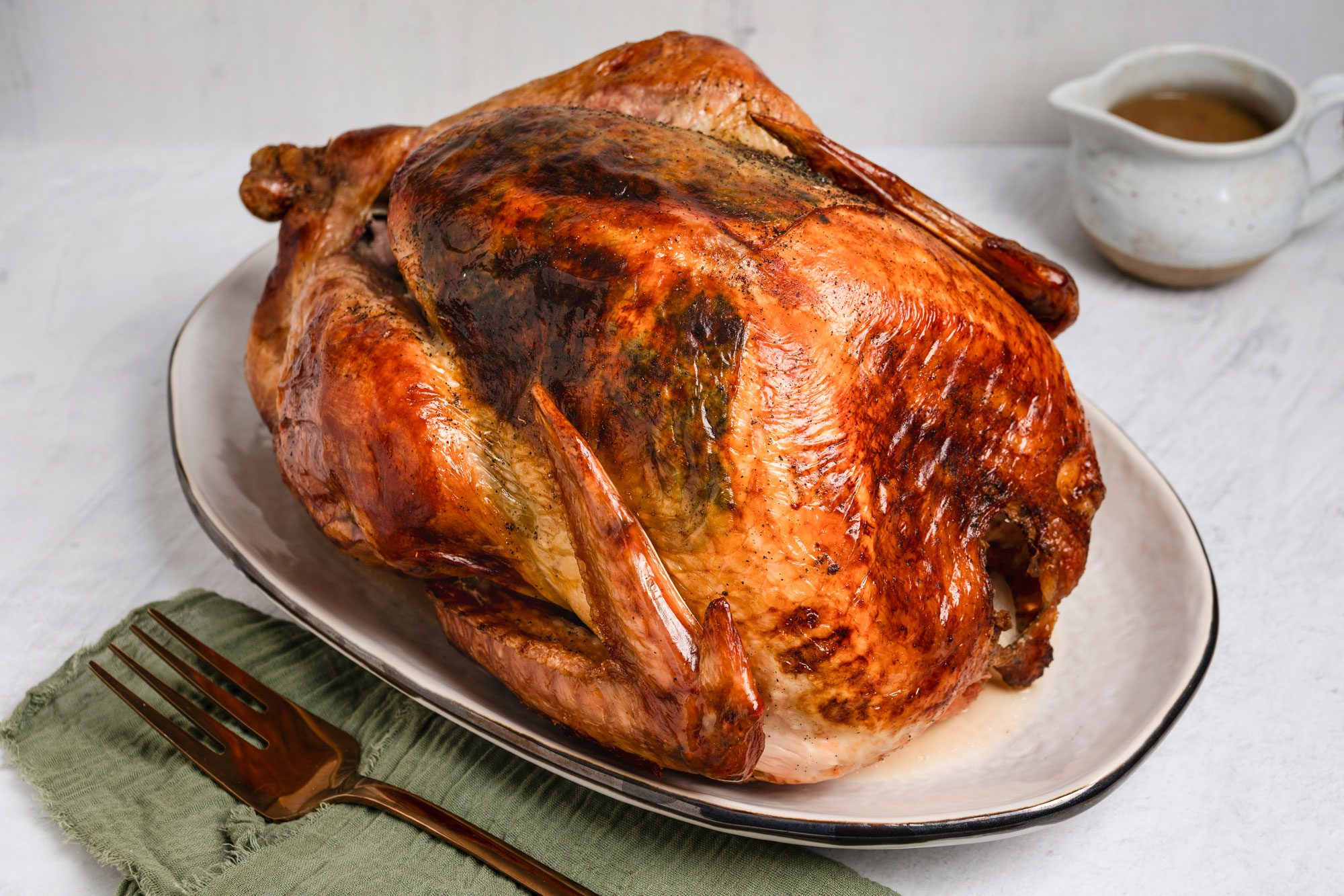 Close shot of Classic Cheesecloth Turkey; served on a large plate with gravy in a jar; a green napkin and a fork; marble surface;