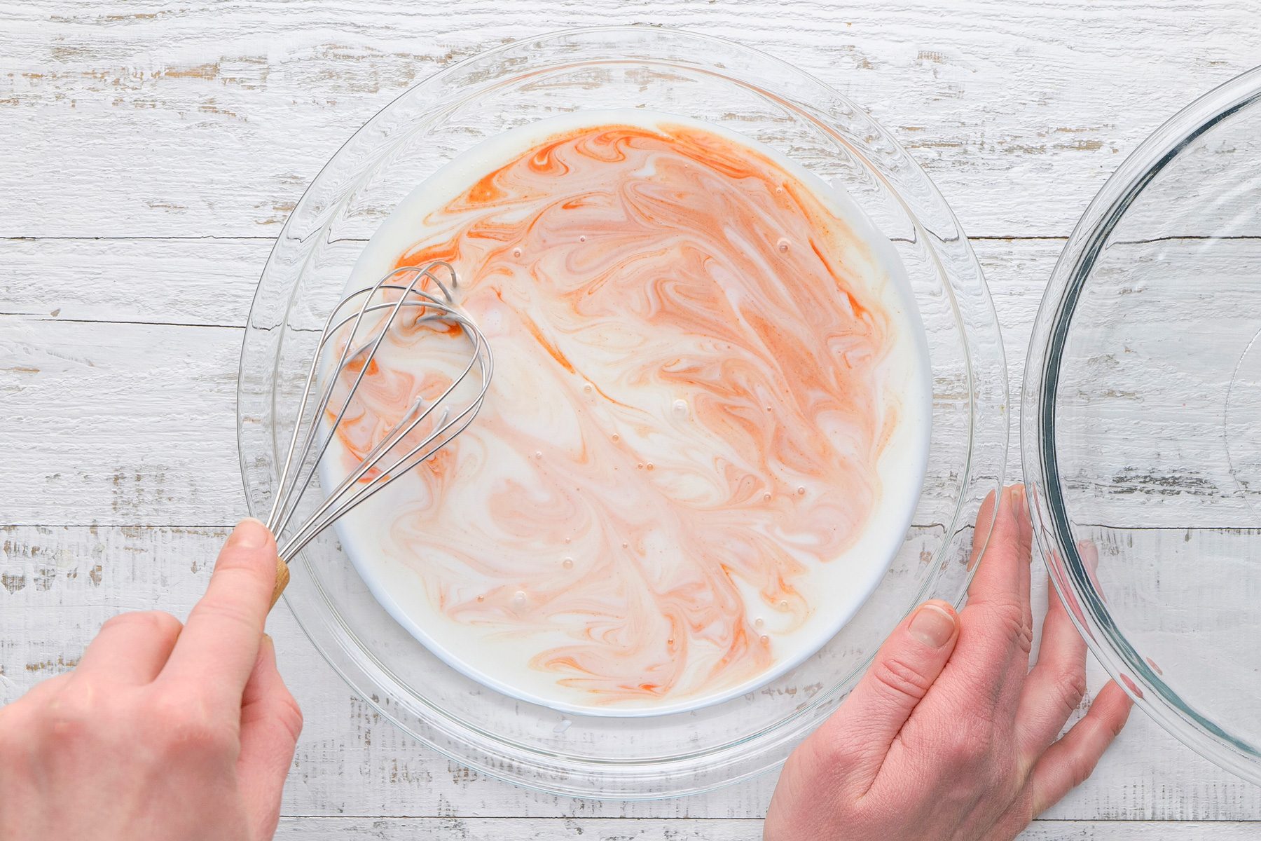 Overhead shot of a shallow bowl; mix buttermilk and hot sauce; white wooden surface;