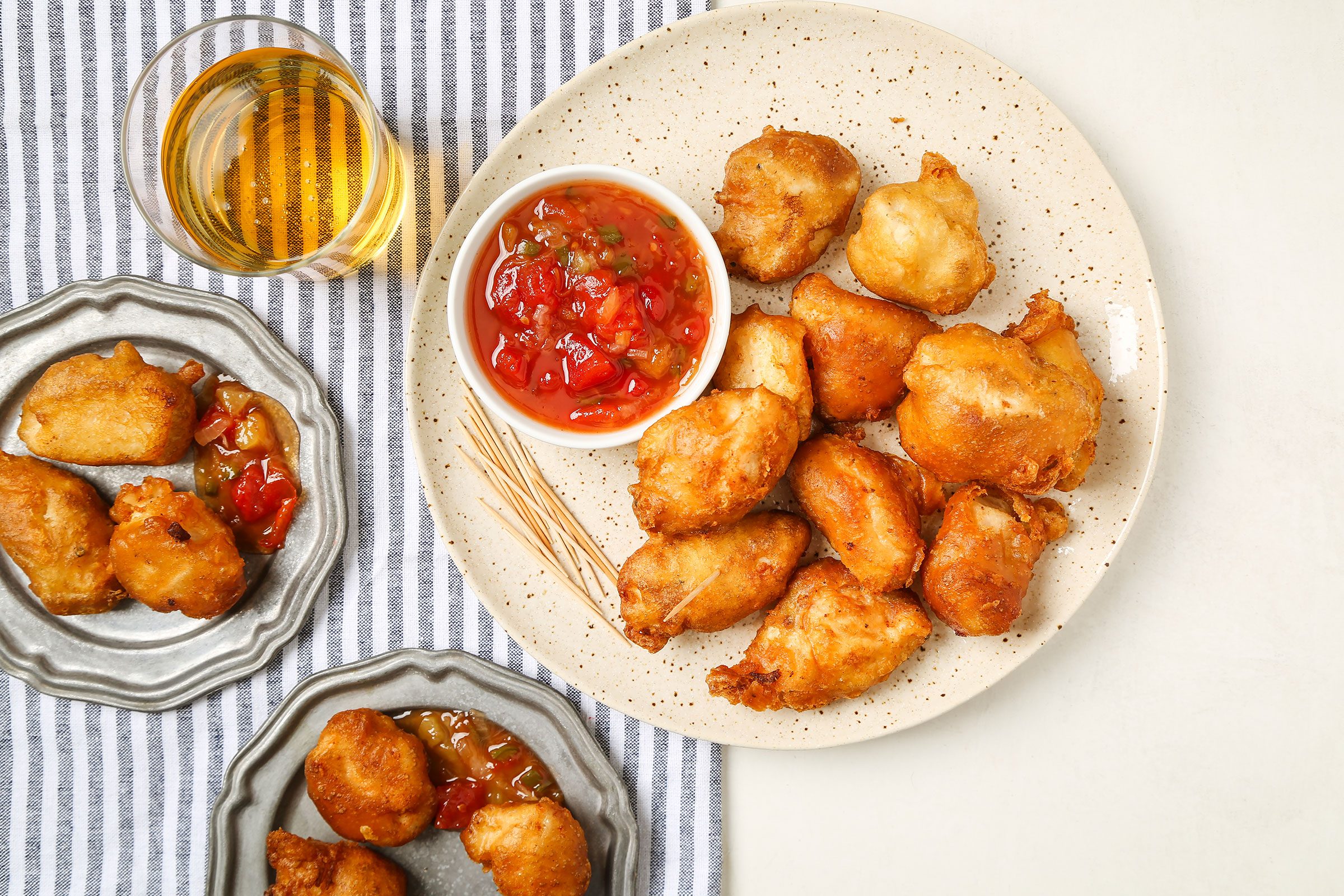 Fried Sweet And Sour Chicken in a cream plate on a striped kitchen towel with a sauce and a beverage on side