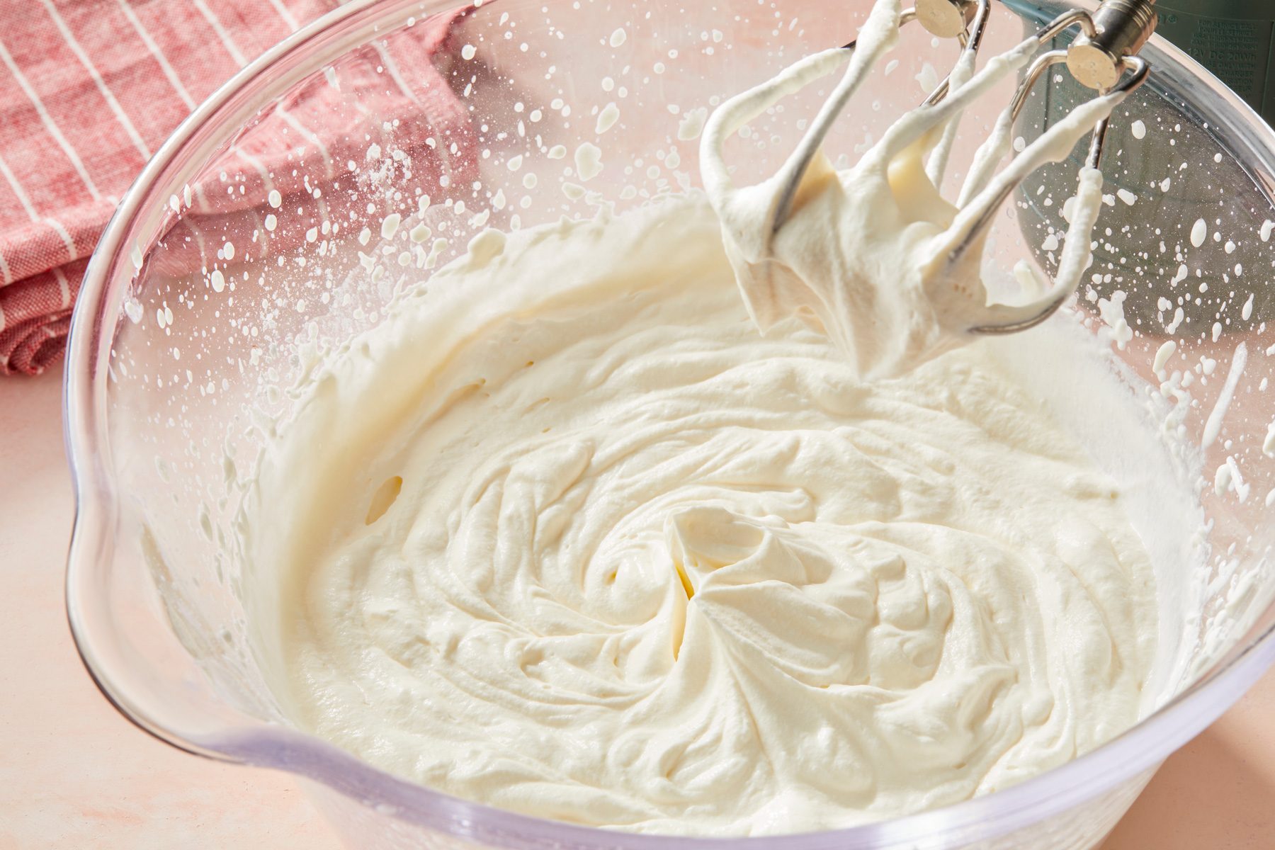3/4th shot of a clear mixing bowl filled with a fluffy, white mixture, a striped kitchen towel in shades of red and white in the background
