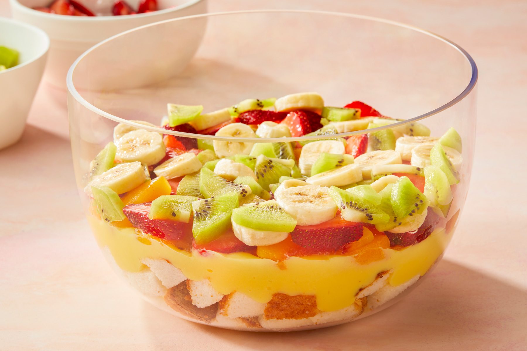 horizontal shot of fruit salad presented in a large, clear bowl; the background shows additional bowls containing more fruits
