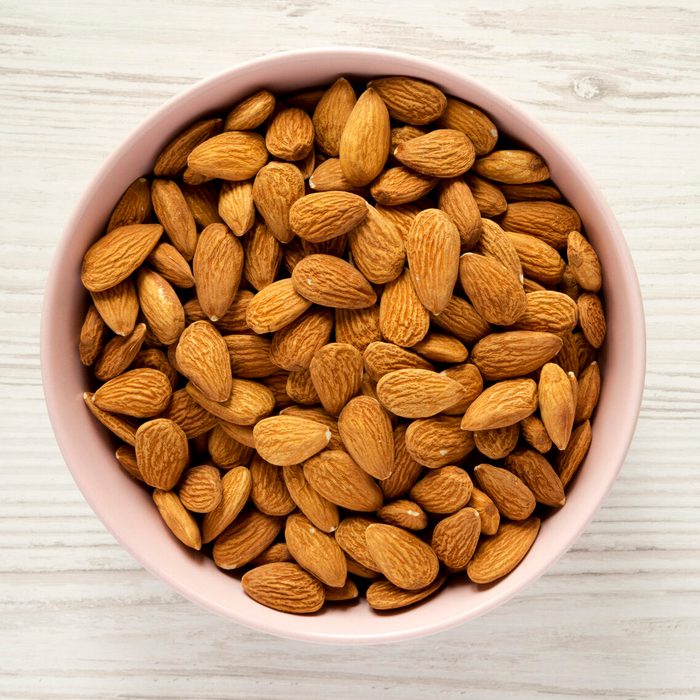 Full pink bowl of almonds over white wooden background, overhead view. Flat lay, from above, top view. Close-up.