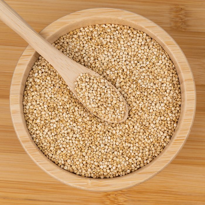 Quinoa seeds in a wooden bowl with a spoon on a bamboo surface