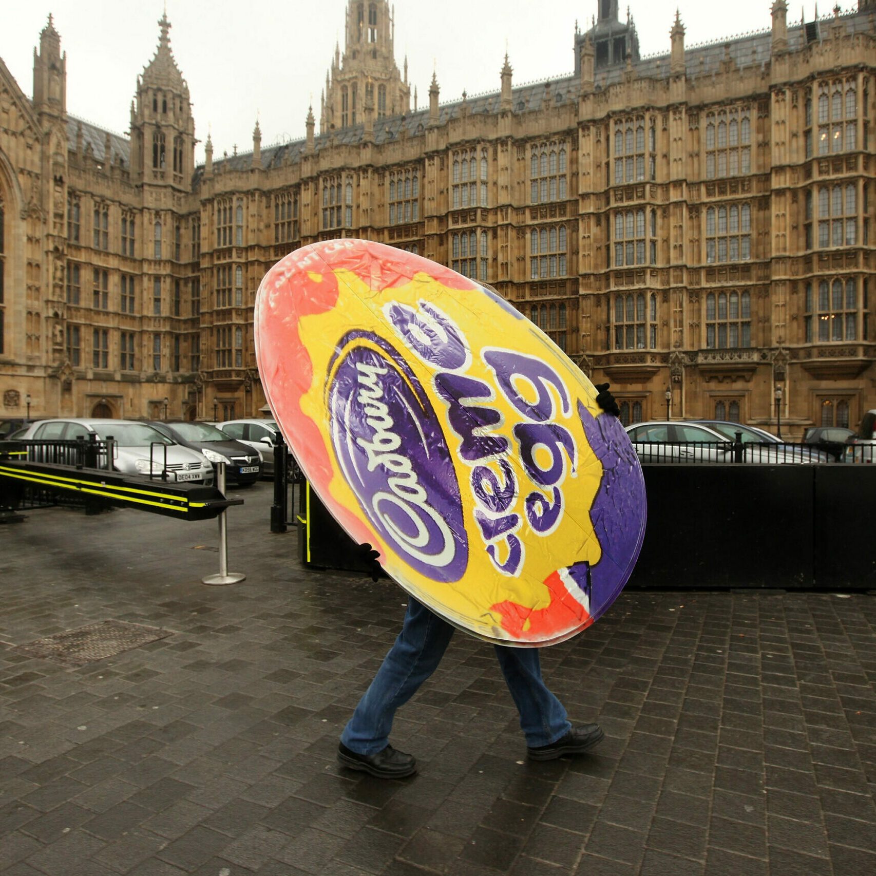 Person holds a Cadbury Creme Egg cutout in front of a British parliament building