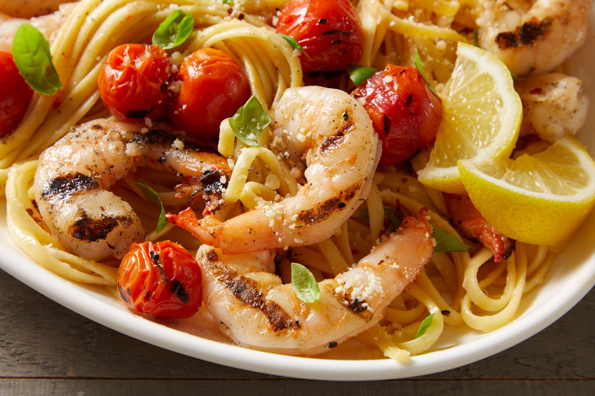 closeup shot of Grilled Shrimp & Tomatoes with Linguine in a white oval platter filled with a generous serving of linguine topped with grilled shrimp skewers and roasted cherry tomatoes