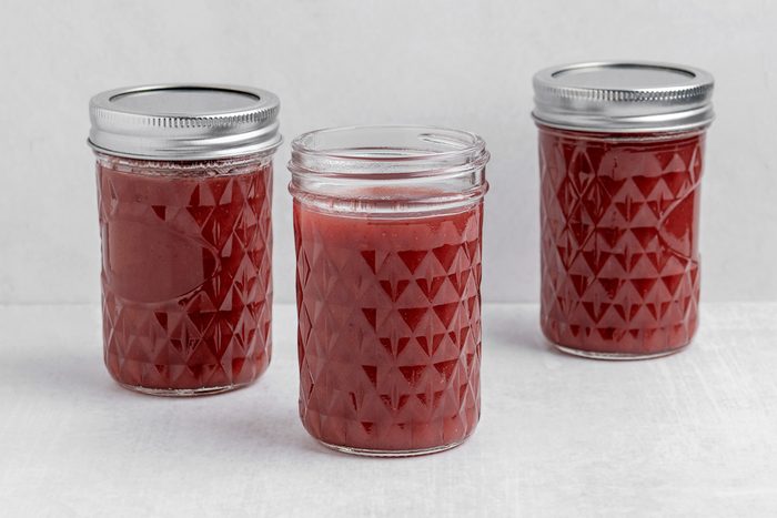 Three glass jars with a diamond pattern are filled with reddish-pink liquid. Two jars have metal lids, while the jar in the center is open. The jars are placed on a light-colored surface.