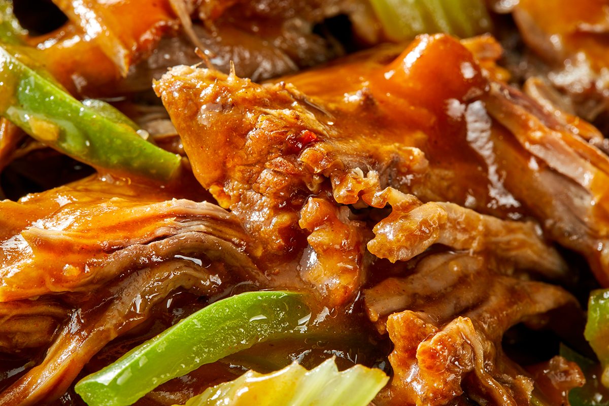 Close-up of tender, shredded beef in a rich brown sauce, mixed with sliced green bell peppers and cooked onions. The dish appears savory and well-seasoned.