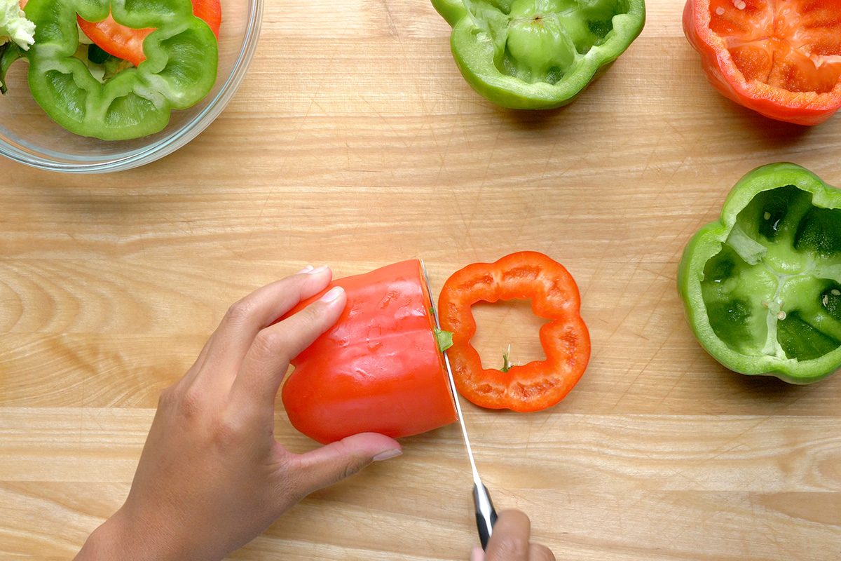 overhead shot of a person is cutting a red bell pepper in half on a wooden cutting board, The pepper is bright red and has been sliced lengthwise