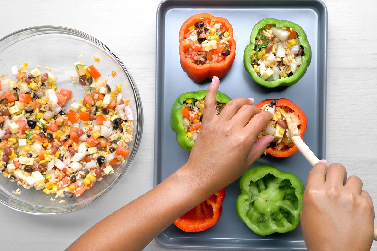 overhead shot of a baking sheet with several bell peppers being stuffed with a mixture of ingredients, The peppers are red and green, and they have been cut in half and hollowed out, The filling appears to be a mixture of rice, vegetables