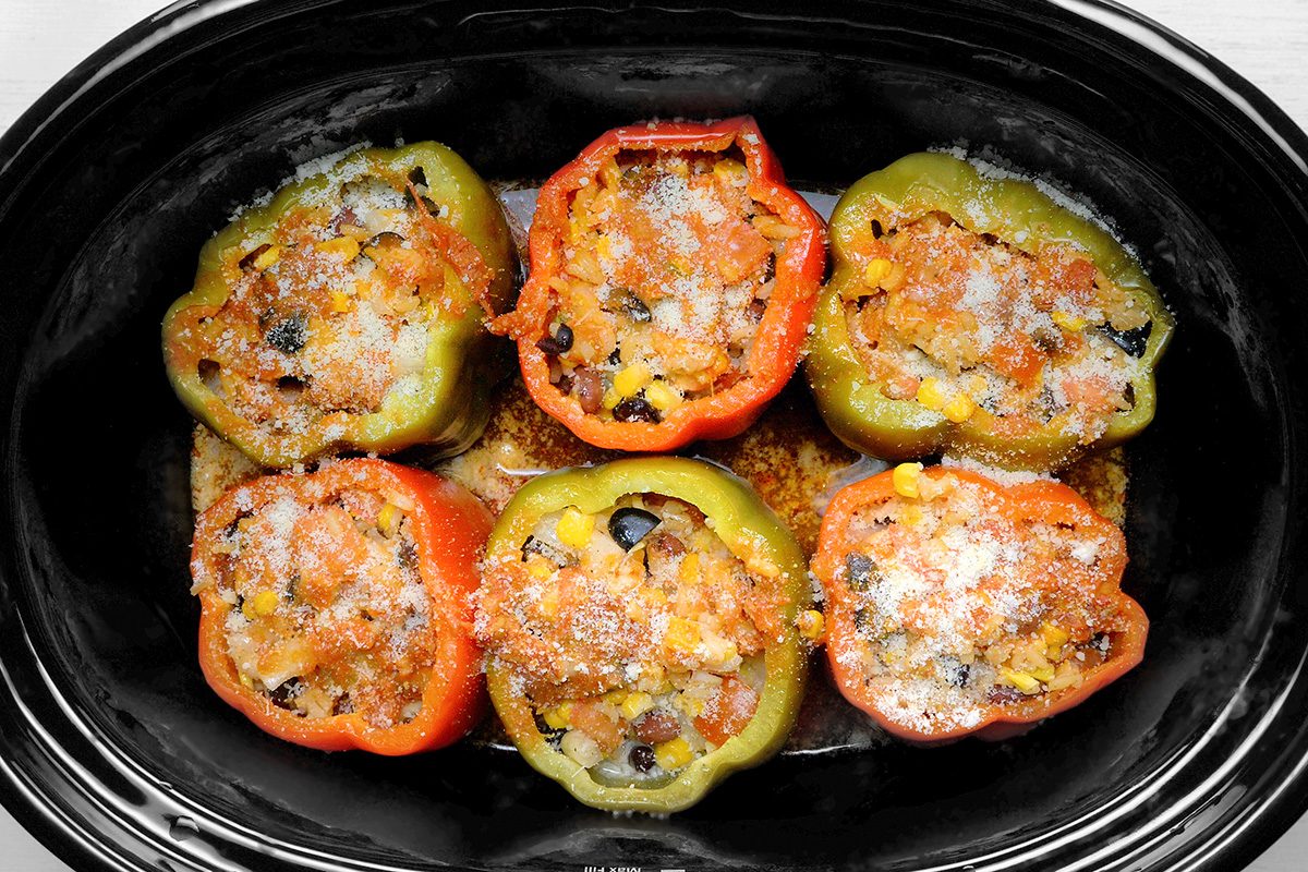 overhead shot of a slow cooker filled with stuffed bell peppers, The peppers are red and green, and they are filled with a mixture of rice, vegetables, The peppers are topped with shredded cheese