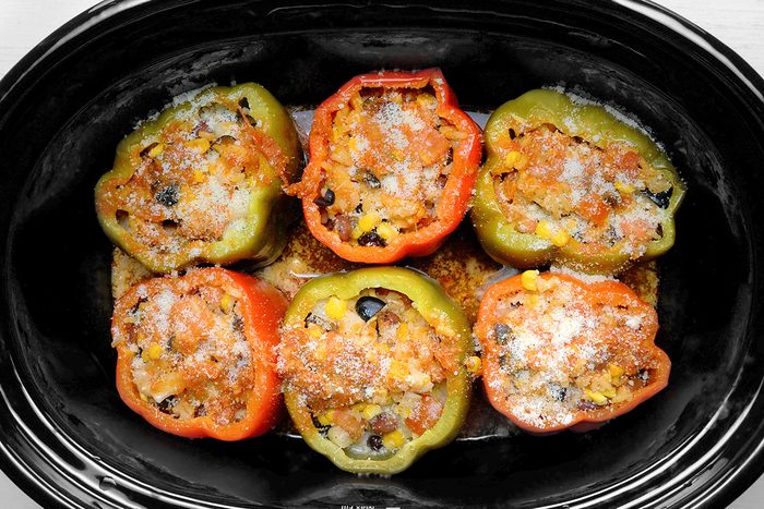 overhead shot of a slow cooker filled with stuffed bell peppers, The peppers are red and green, and they are filled with a mixture of rice, vegetables, The peppers are topped with shredded cheese