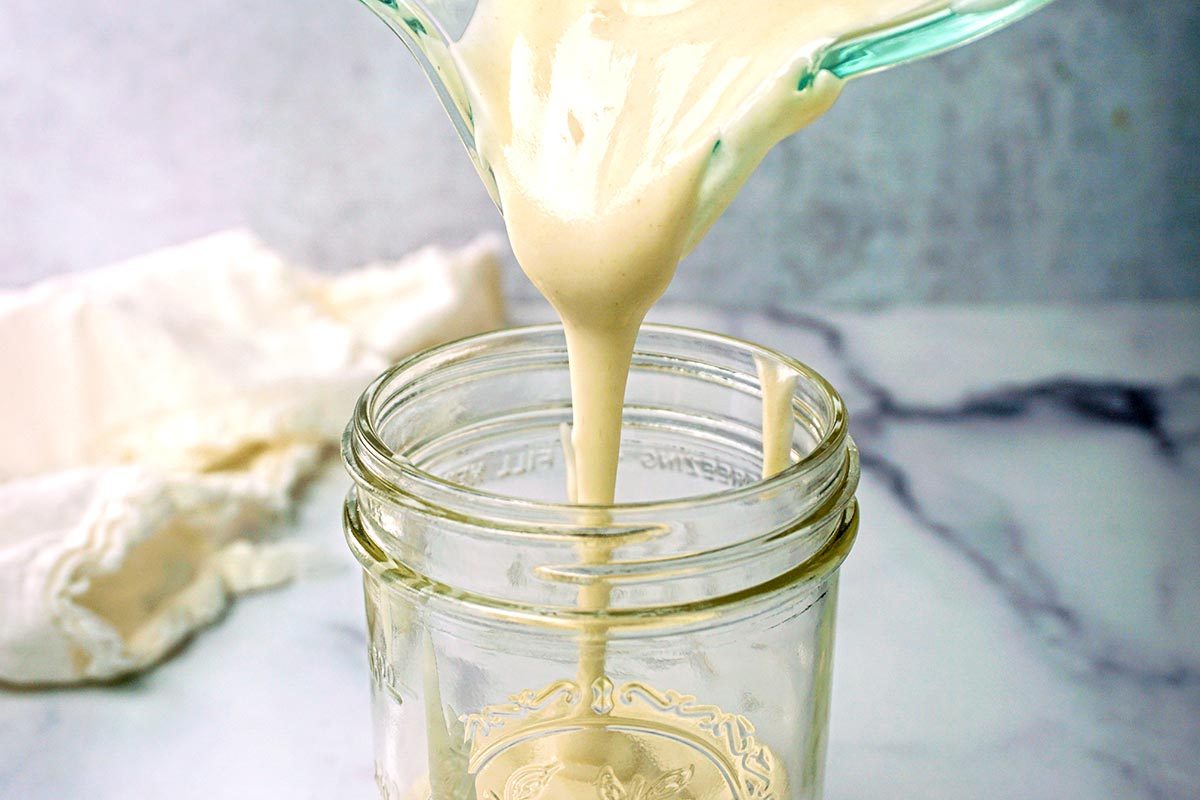 Homemade cooking spray mixture being poured from a bowl into a mason jar