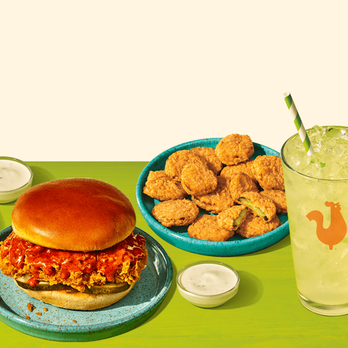 Chicken sandwich, fried pickles, and green iced lemonade on a green table