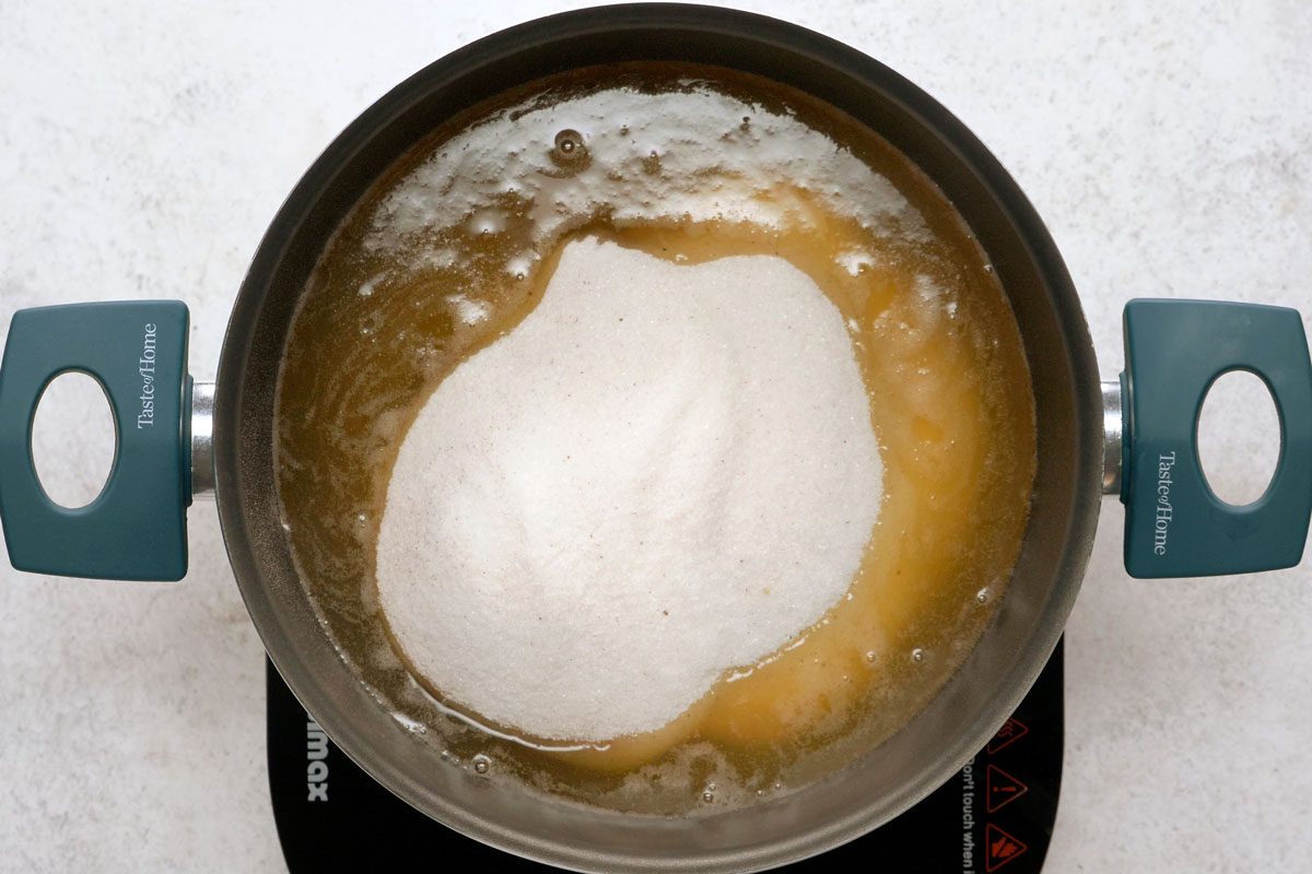 overhead shot of a pot with a green handle is on the stovetop; inside the pot is a mixture of brown liquid and white sugar; the pot is on a black burner, the burner is on a white countertop;