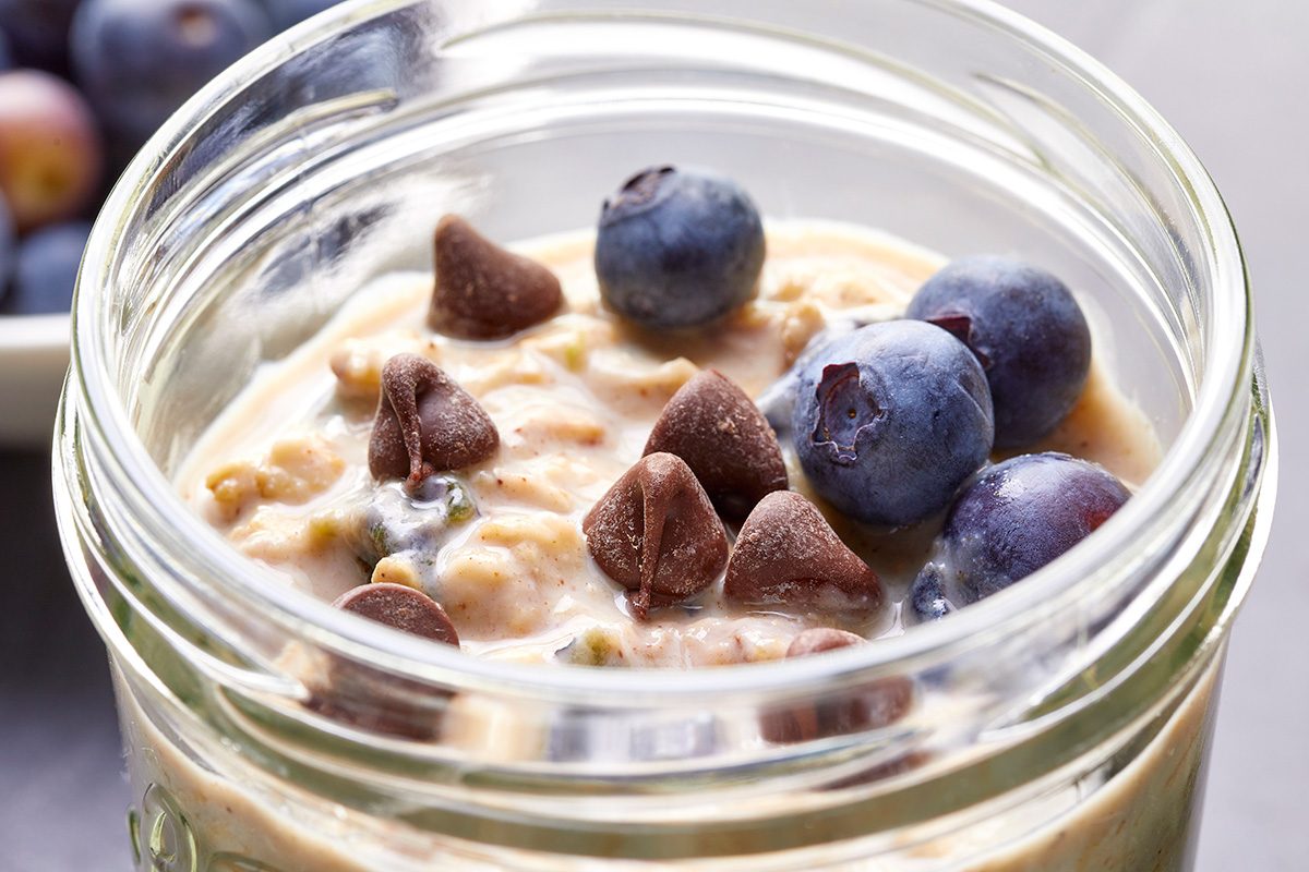 Close-up shot of Blueberry Overnight Oats in a glass jar; served with chocolate chips; granola; and additional berries on top