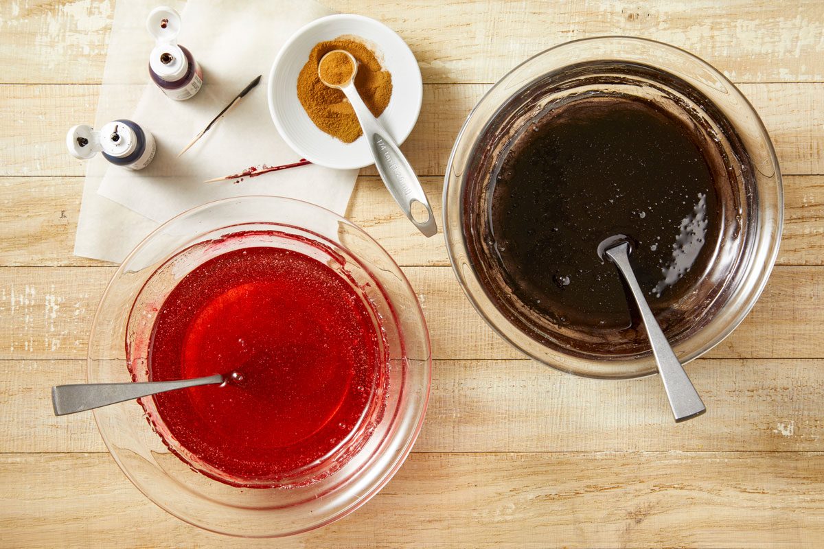 Overhead shot of remove from the heat and pour into 2 small bowls; Stir 1/4 teaspoon cinnamon and red food coloring into 1 bowl; stir black food coloring and remaining cinnamon into other bowl; light brown surface;