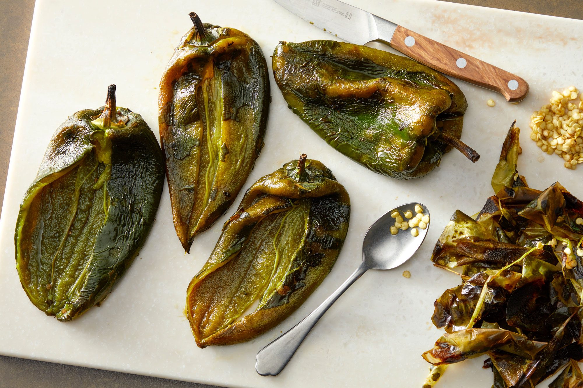 Close shot of peel off and discard charred skin; Cut a slit lengthwise down the peppers; discard seeds; on a chopping board; all set on a light brown surface
