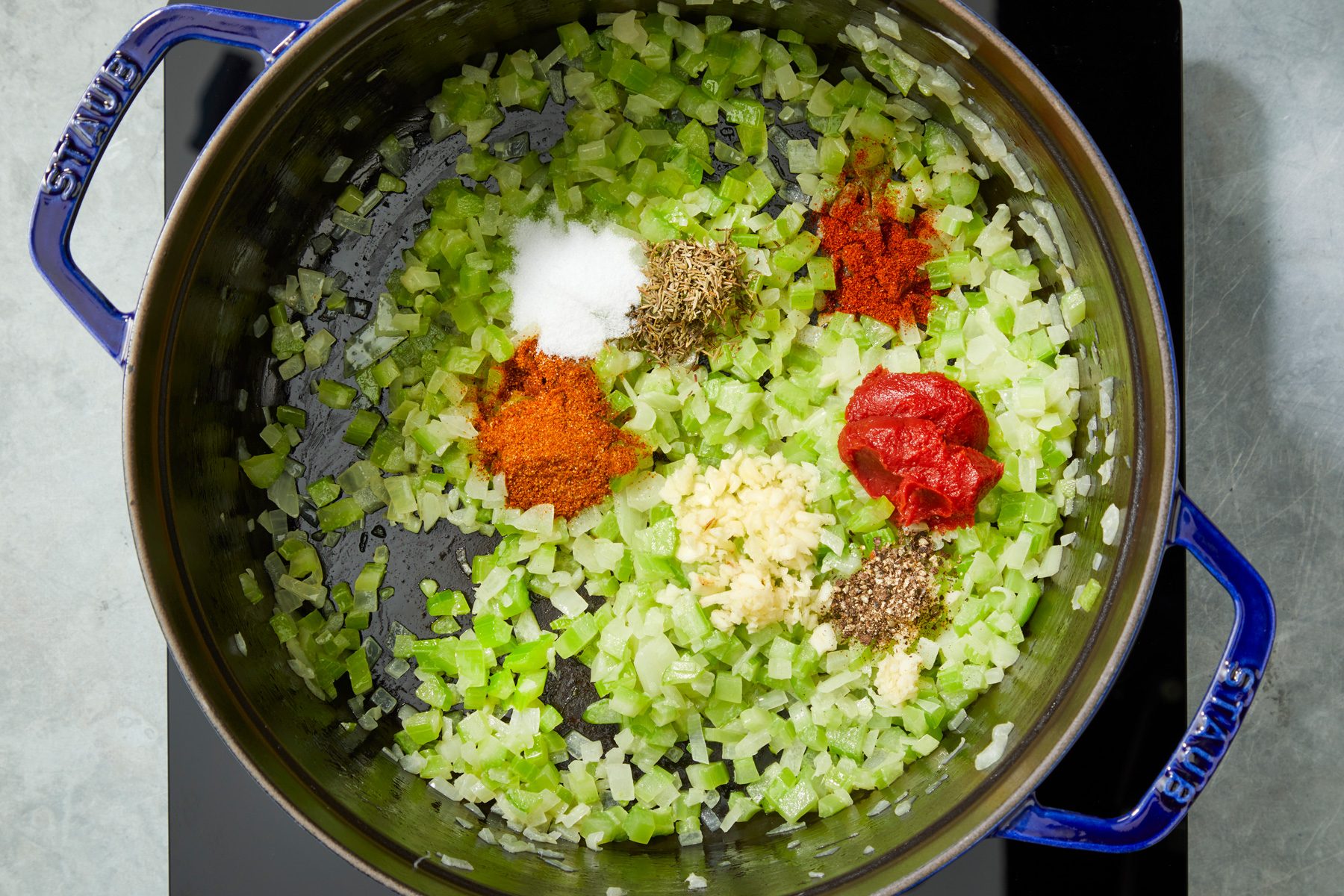 Overhead shot of the same saucepan stir in garlic; tomato paste; salt; Old Bay seasoning; thyme; pepper and cayenne; cook one minute longer; induction; grey surface;