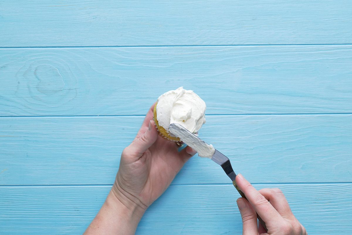 Overhead shot of Cream Cheese Frosting; apply on cup cake with knife; blue wooden surface