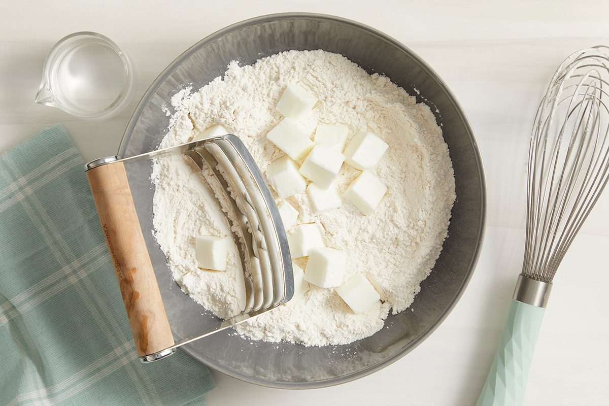 Overhead shot of a bowl mix flour and salt; cut in shortening until crumbly; whisk tool; napkin; cream surface