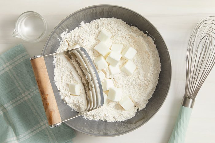 Overhead shot of a bowl mix flour and salt; cut in shortening until crumbly; whisk tool; napkin; cream surface
