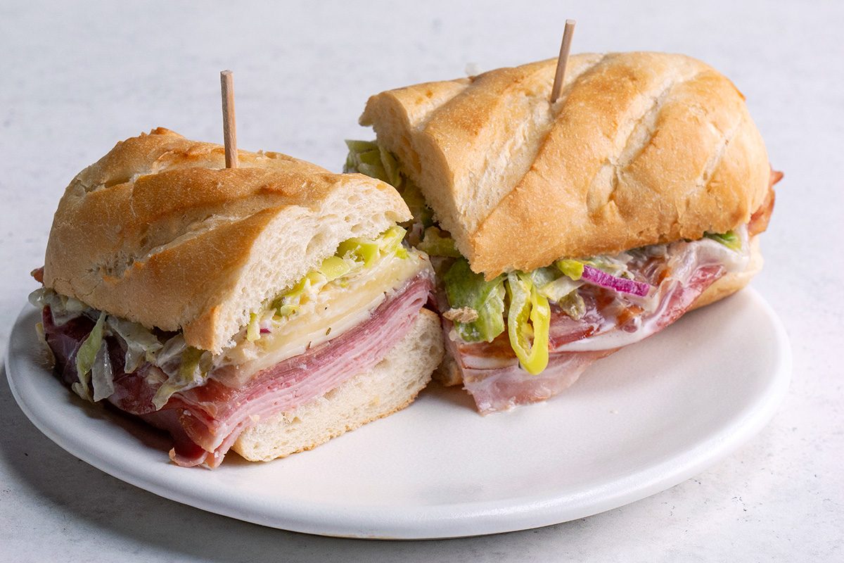 Grinder Sandwich close up shot showing all it layer of veggies and meat on a nice wihte plate 