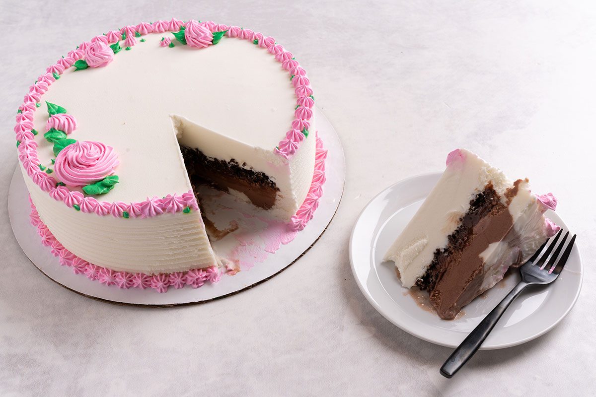 White ice cream cake with pink icing detailing and a slice cut out of it on a plate with a fork