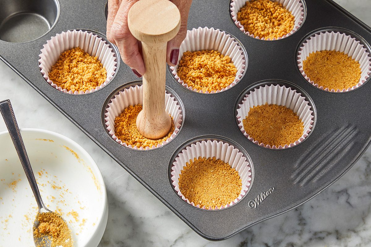 High angle view shot; Preheat oven to 350 degree; In a small bowl combine graham cracker crumbs and butter; Divide the mixture evenly among 9 paper-lined muffin cups; Gently press the mixture into the bottoms of the liners using a wooden tool; marble surface