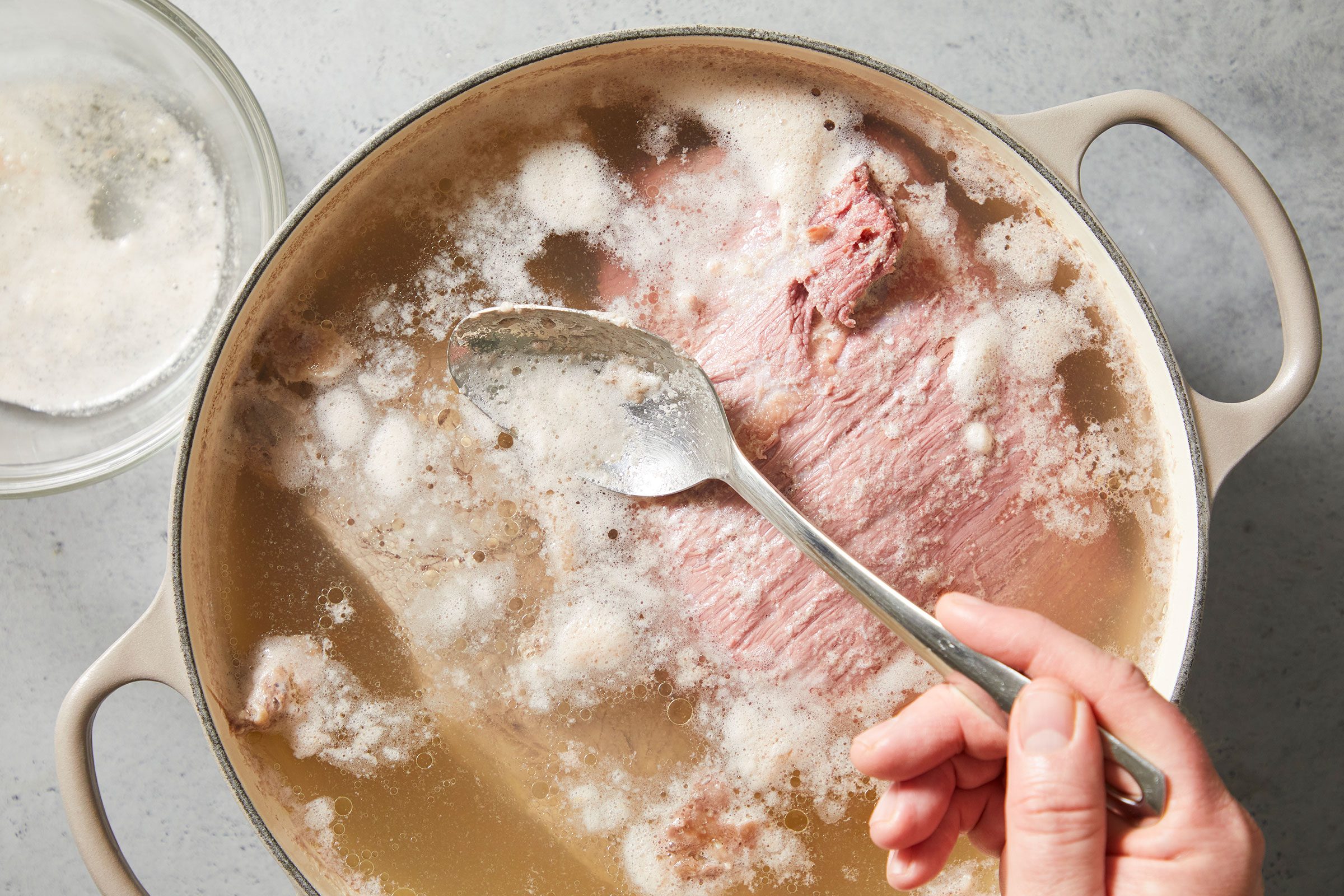 Discarding any foam that rises to the top of simmering meat in water