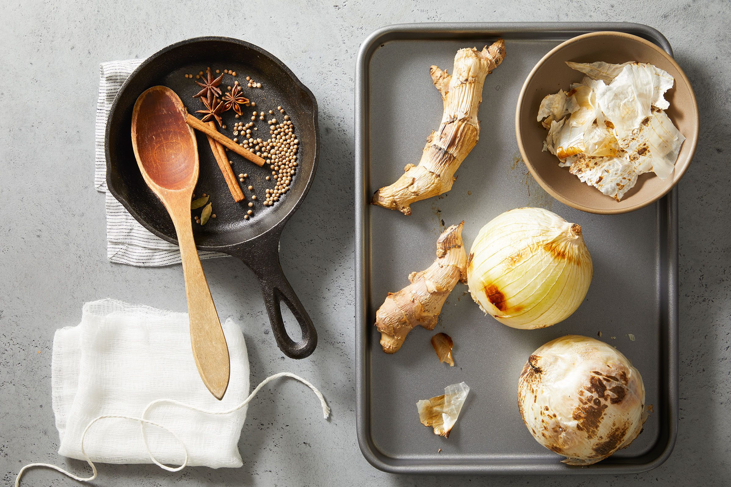 Slightly roasted and charred onion and ginger on an ungreased baking sheet with a small skillet on side having dry spices in it