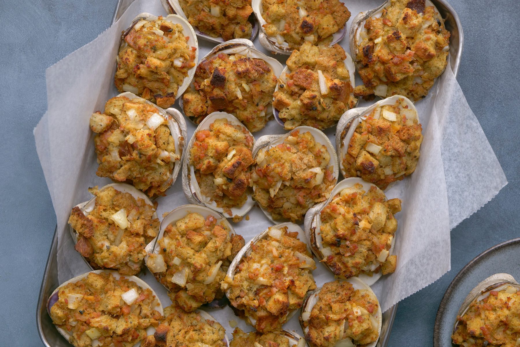 overhead shot of Rhode Island Stuffies are presented on a silver baking sheet lined with parchment paper; a few more stuffies are visible on a separate gray plate in the lower right corner of the image, and the background is a gray surface