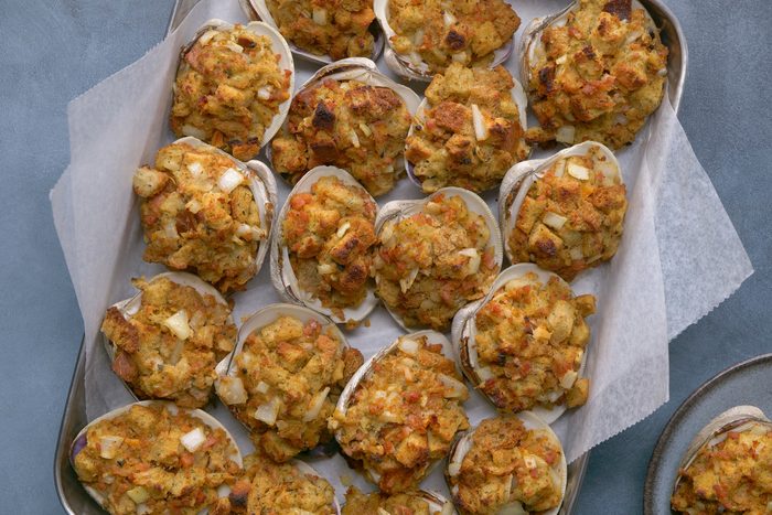 overhead shot of Rhode Island Stuffies are presented on a silver baking sheet lined with parchment paper; a few more stuffies are visible on a separate gray plate in the lower right corner of the image, and the background is a gray surface