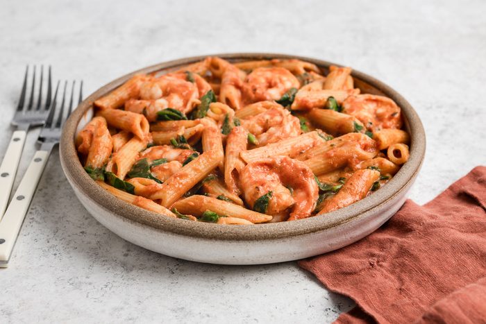 Spicy Shrimp And Penne Pasta with spinach in a bowl and some cutlery placed on side.