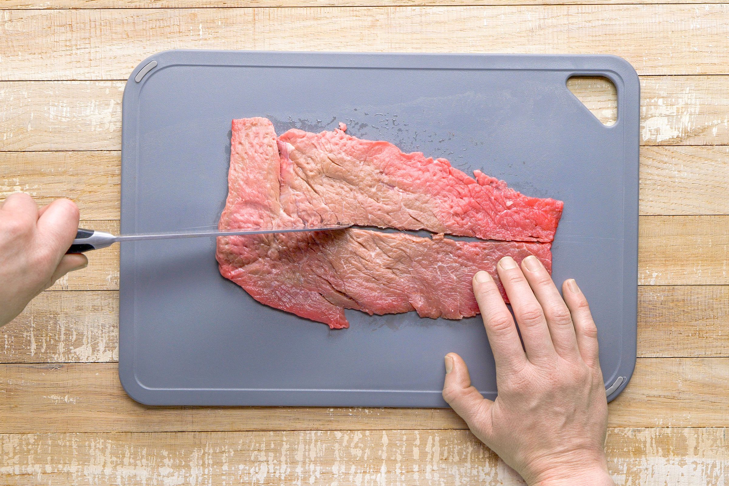 Slicing the flattened meat into small pieces on a board with a knife.