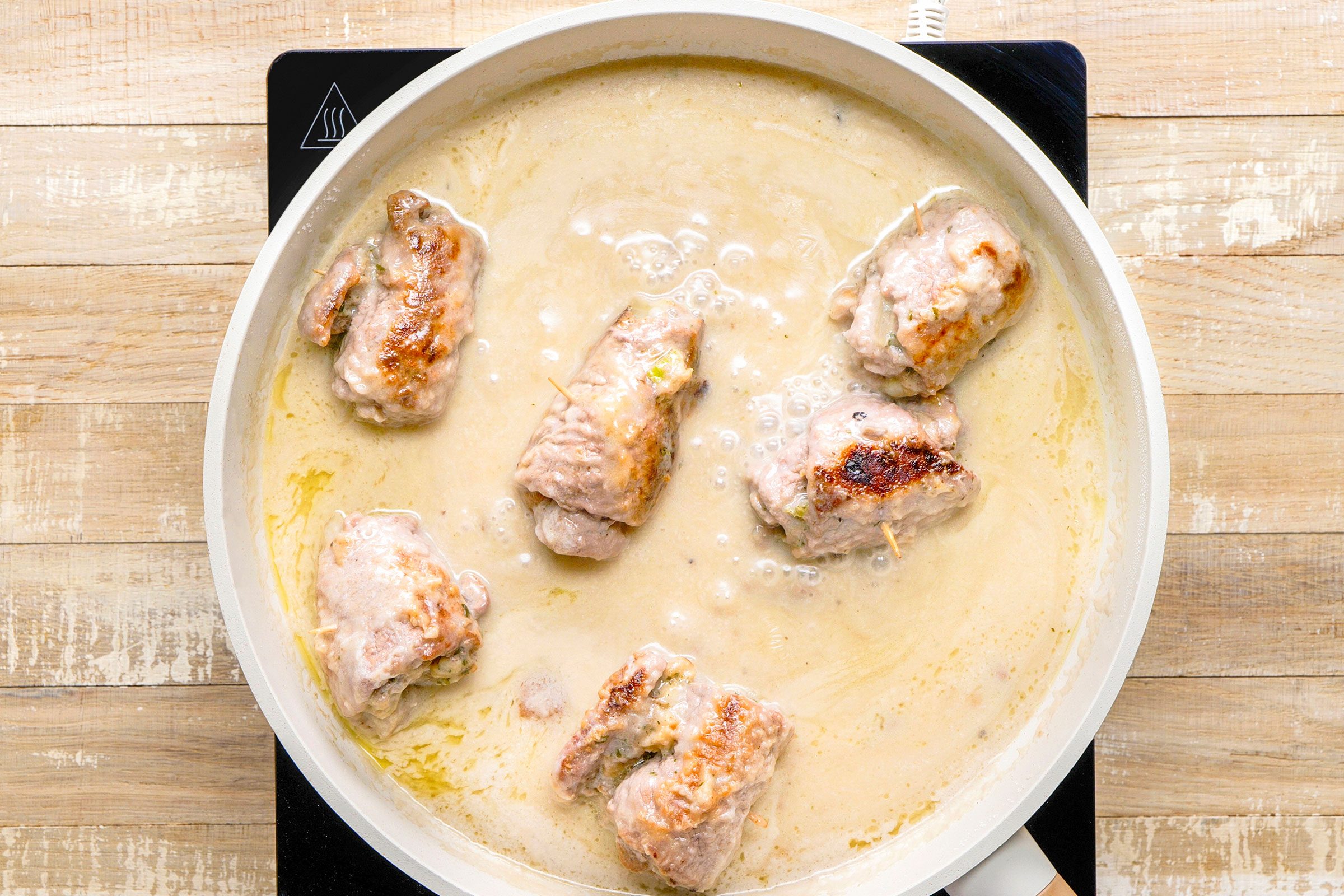 Cooking meat rolls in sauce in a skillet on induction.