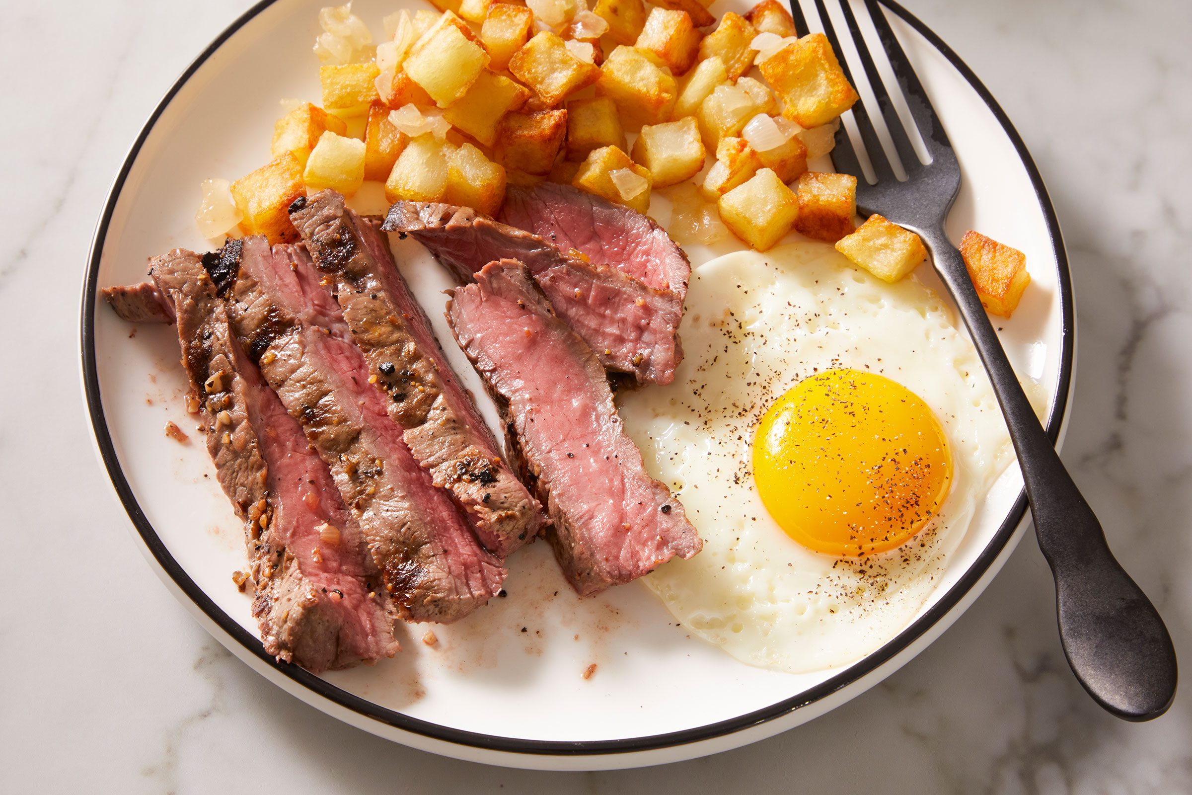 Served some sliced steak with the eggs and potatoes in a white plate with a fork.