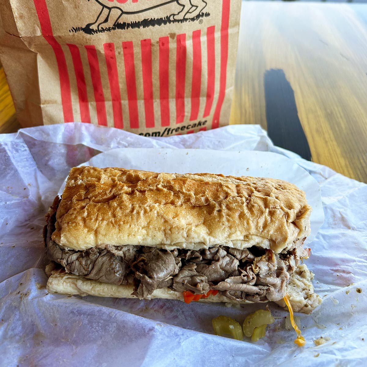 Italian beef sandwich with a red striped takeout back in the background