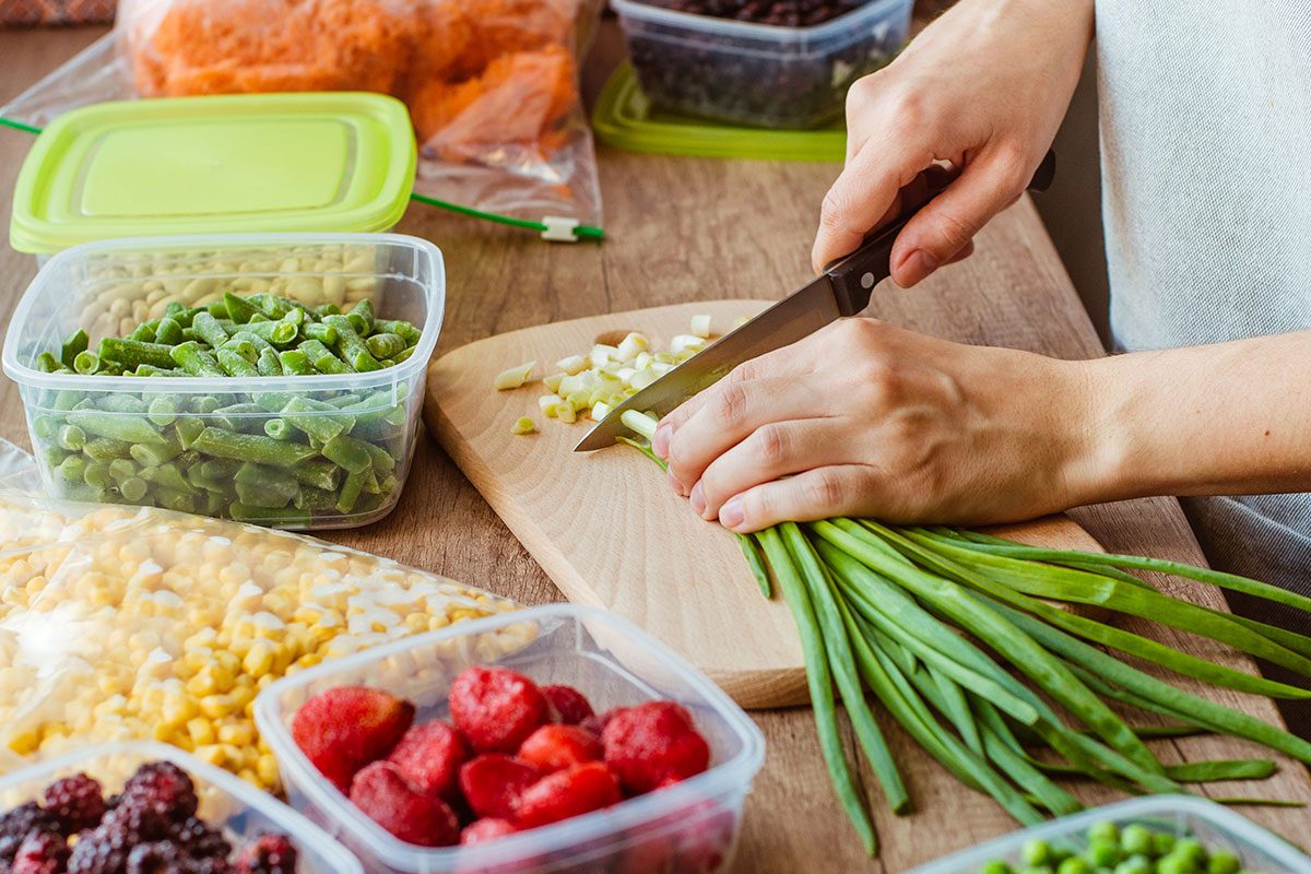 Close up of woman cutting green onion for freezing in the plastic food box