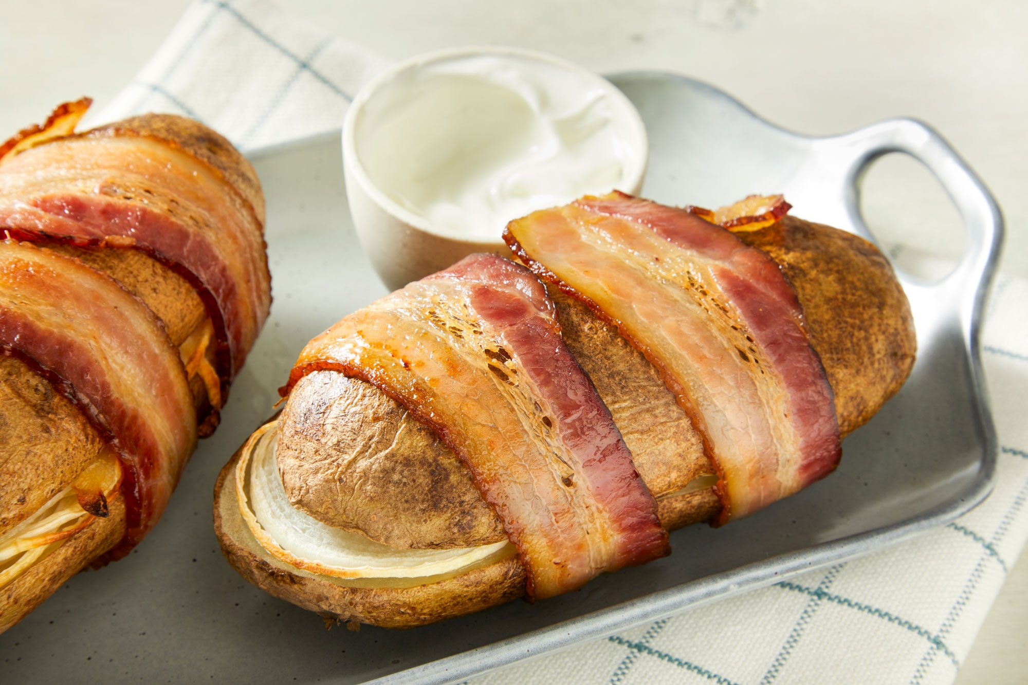 Close-up shot of Bacon-Wrapped Potatoes; served on a tray with choice of dip or sauce on a napkin; all set on a marble surface