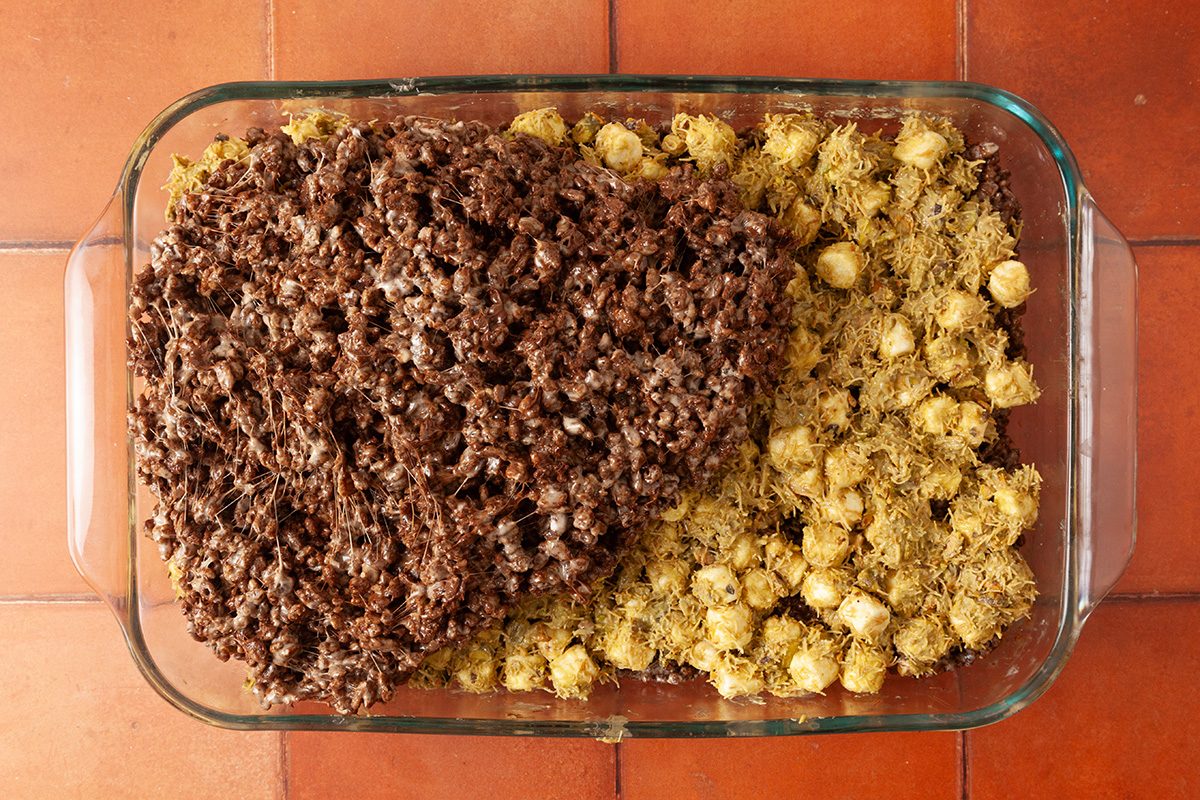 A glass baking dish with two types of food: one side has a dark brown, chunky mixture, and the other side has small, round, yellow pieces, all sitting on a reddish tiled surface.