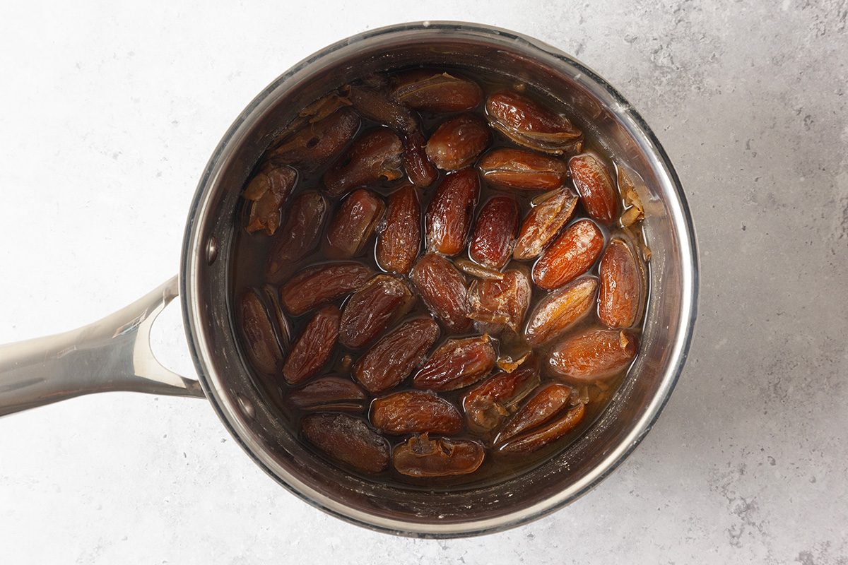 A saucepan filled with whole dates soaking in water, viewed from above on a light-colored surface.