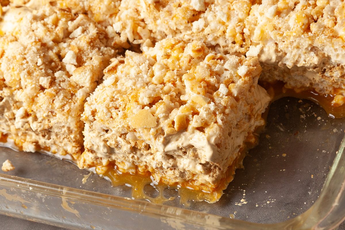 A close-up of a glass baking dish filled with squares of a crumbly dessert, possibly a caramel or nut bar, with a missing piece revealing a gooey layer underneath.