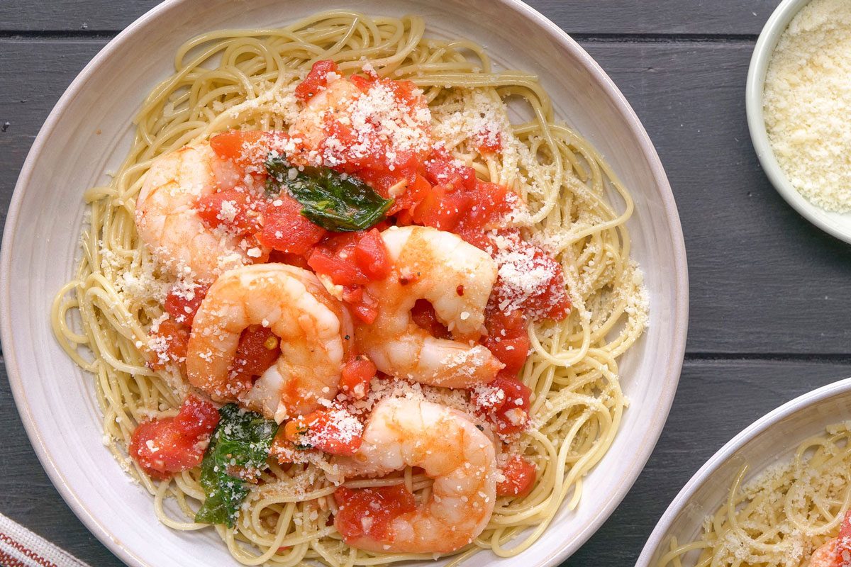 Overhead shot of Shrimp Pomodoro served over spaghetti and topped with cheese in two large bowls; forks rest on a folded napkin nearby; all set on a black wooden surface