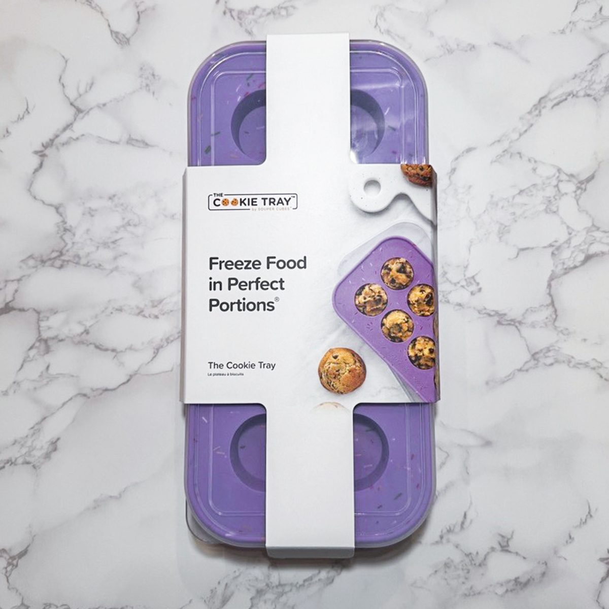 A purple rectangular freezer tray with a white label that reads "Freeze Food in Perfect Portions" and shows images of cookies, lying on a white marble surface.