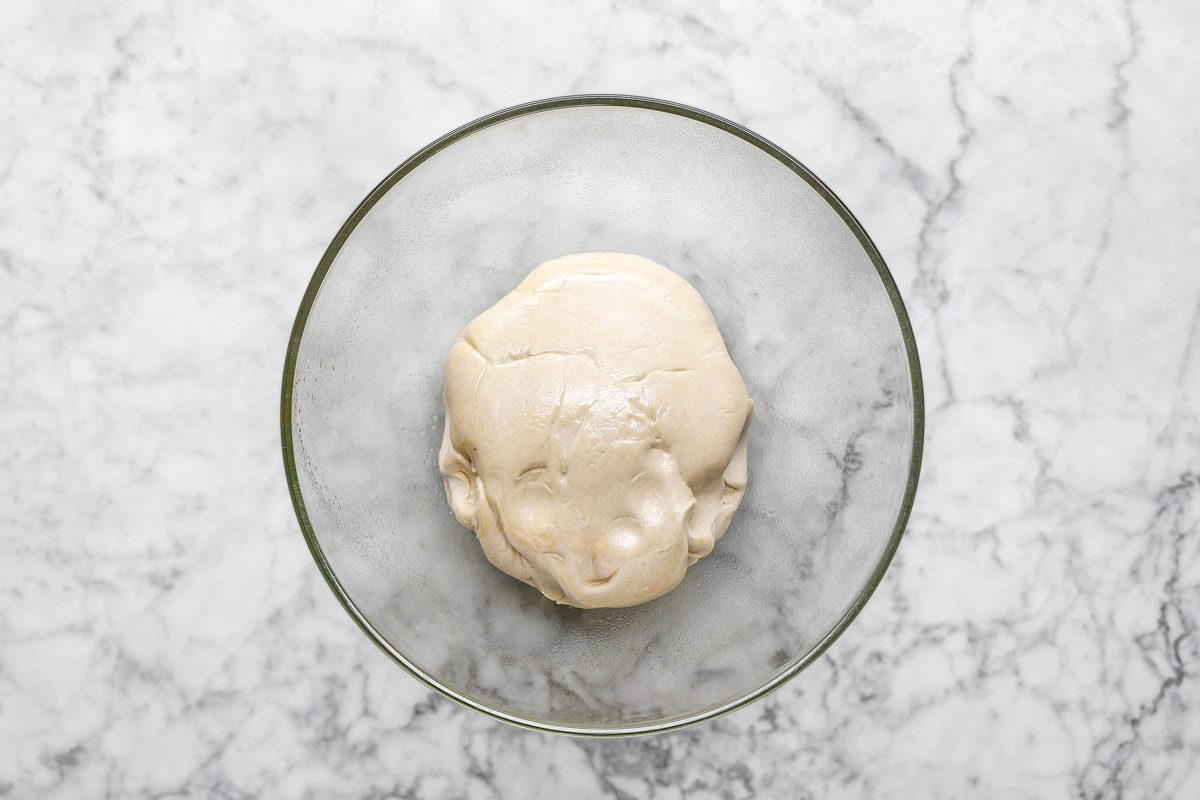 overhead shot of a ball of dough rests in a clear glass bowl on a white marble countertop