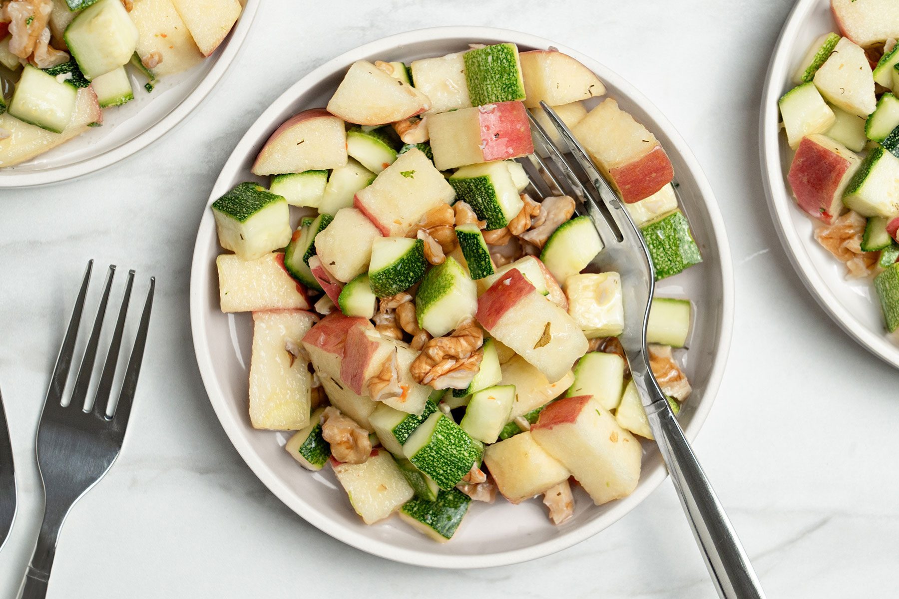 Apple Zucchini Salad in a white bowl with fork kept on side.